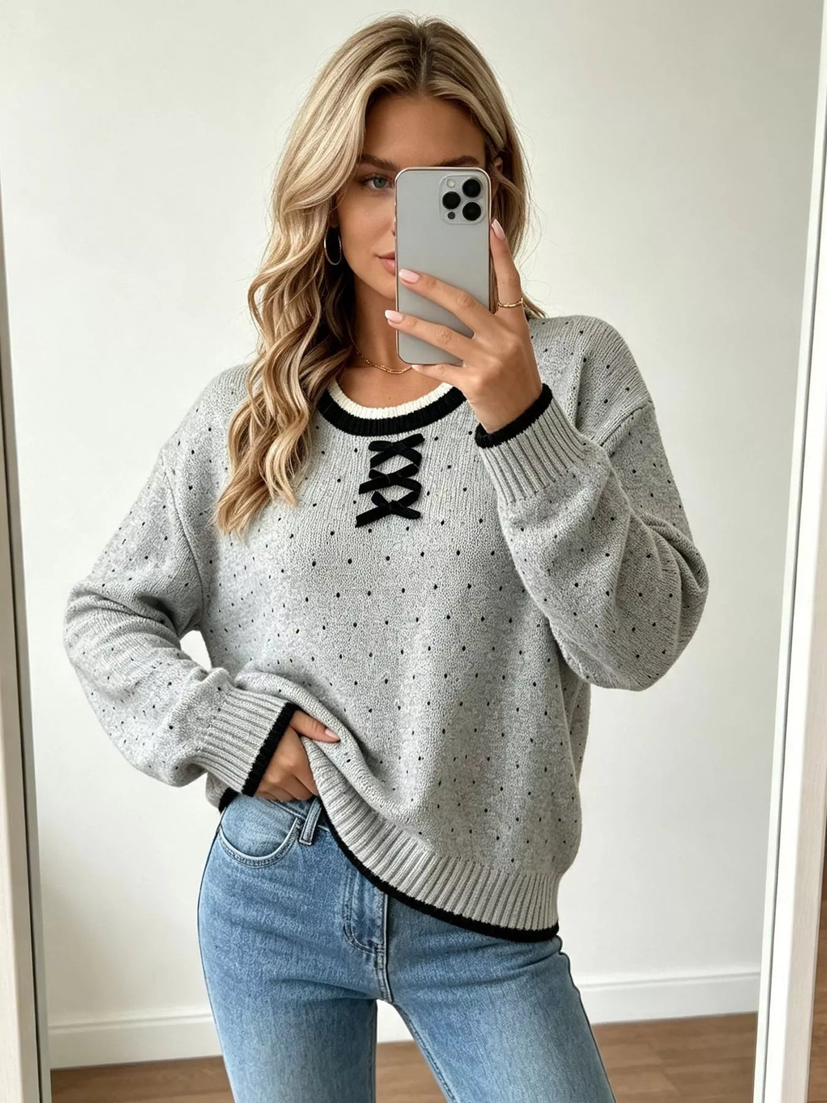 Gray and black polka dot lace-up sweater, front view with raised hand.