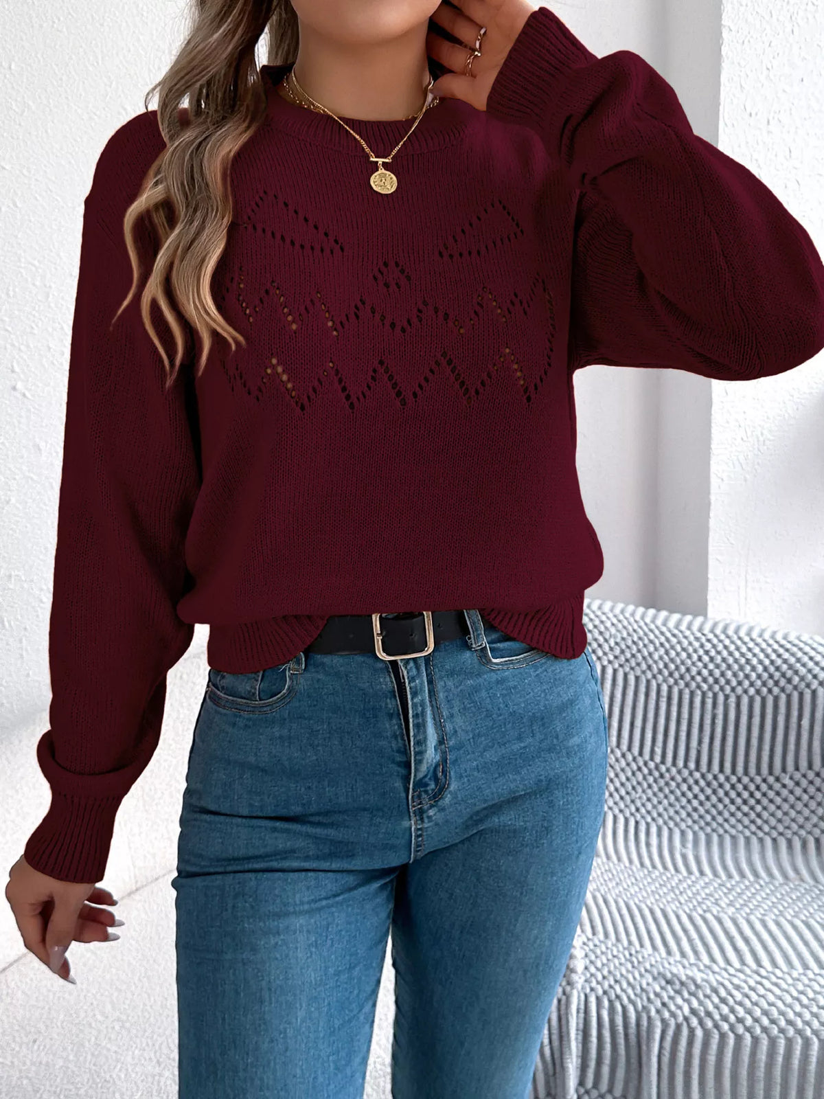 Burgundy halloween pumpkin face knit sweater, front with raised hand.