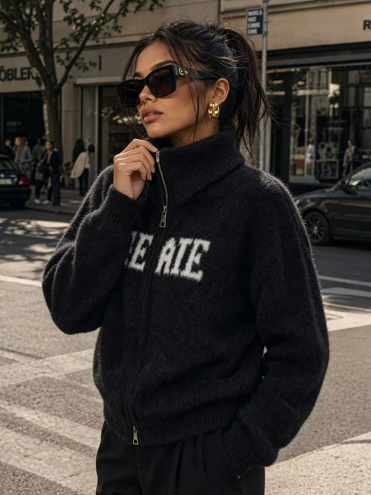 Black fuzzy letter zip-up cardigan, front holding collar.