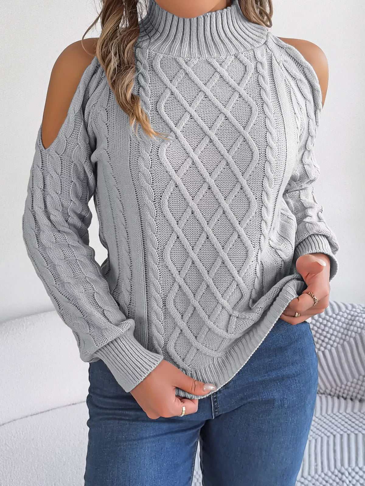 Gray cold-shoulder cable-knit sweater, front holding hem.