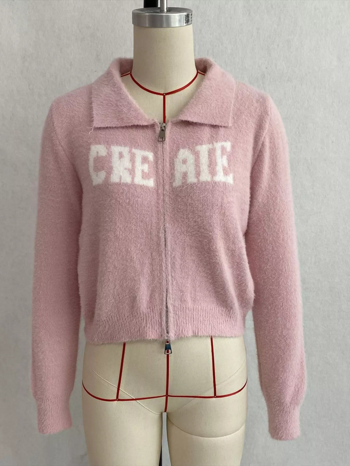 Pink fuzzy letter zip-up cardigan, front on dress form.