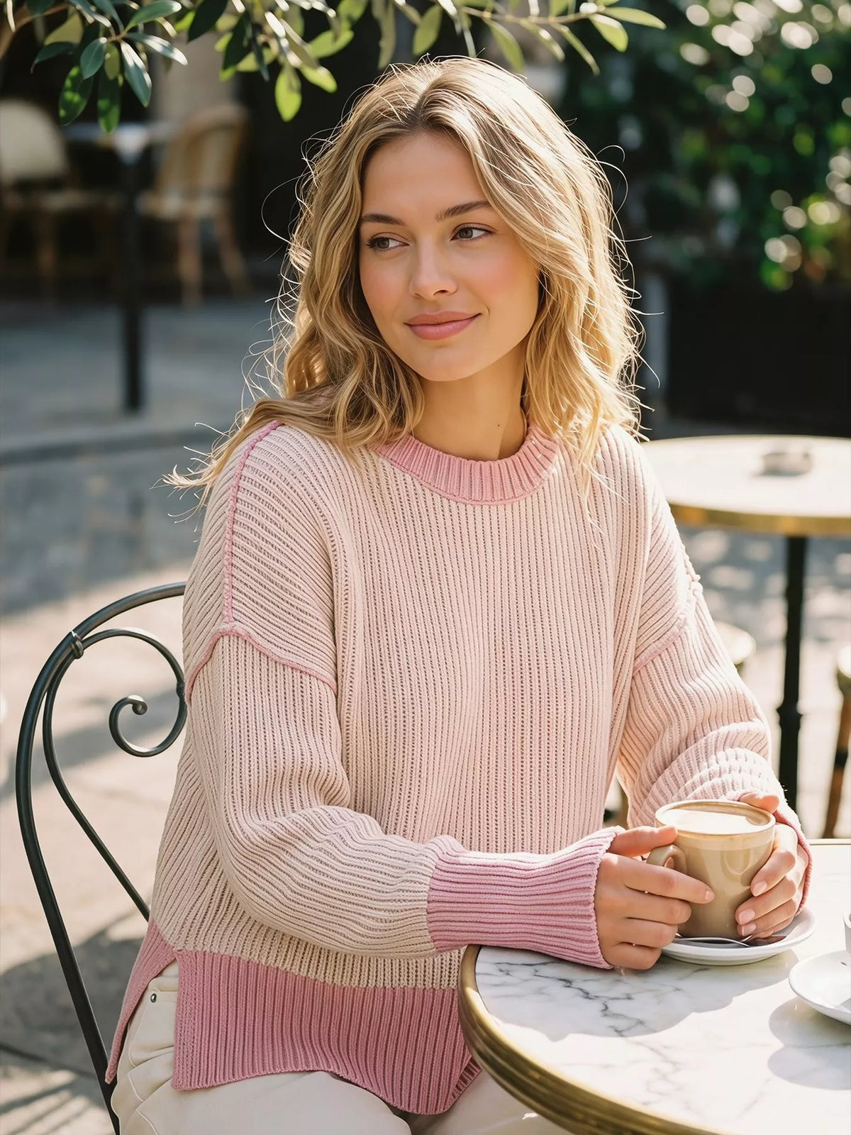Pink ribbed side-slit sweater with contrast trim, seated side view.
