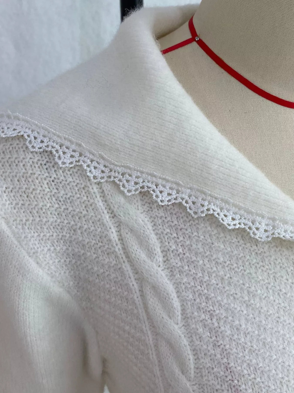 White cable-knit cardigan with lace trim, lace-trim collar close-up.