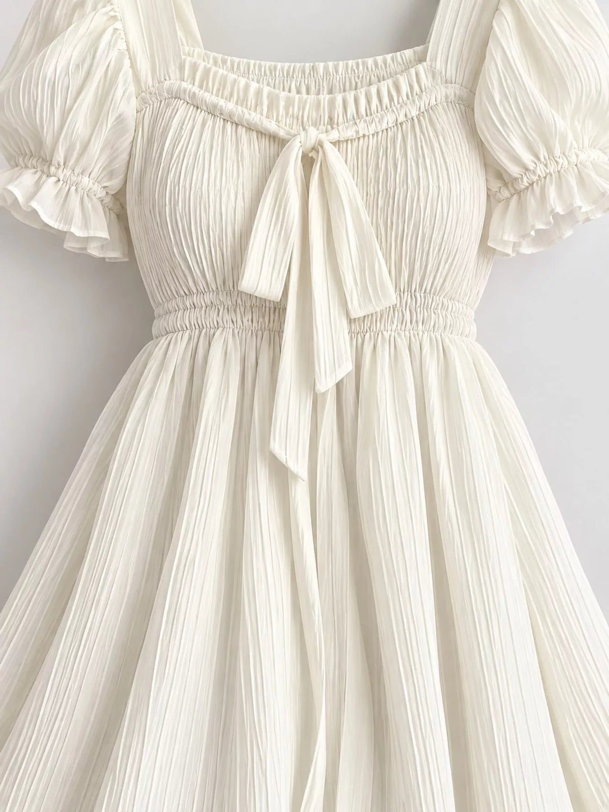 Cream puff-sleeve smocked mini dress with tie-front detail, square neckline, bow, smocked waist, and puff sleeves