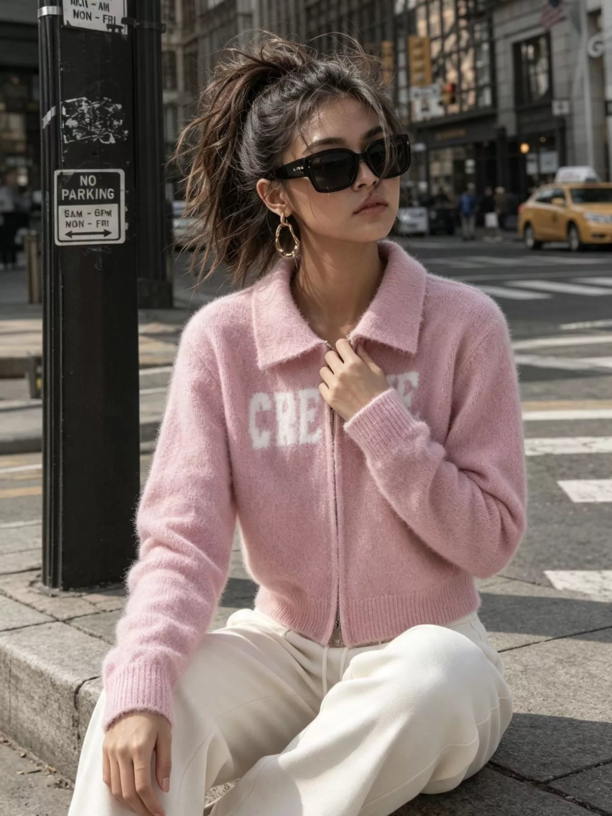 Pink fuzzy letter zip-up cardigan, seated front view.