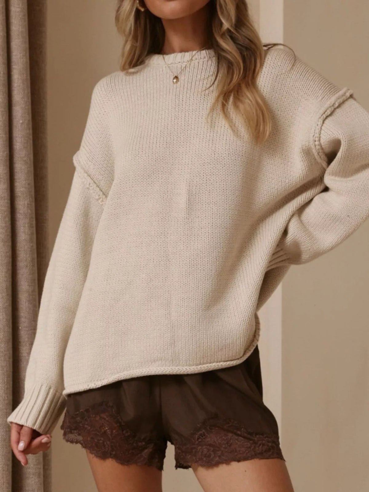Ivory crewneck dropped-shoulder sweater, front with hand at waist.