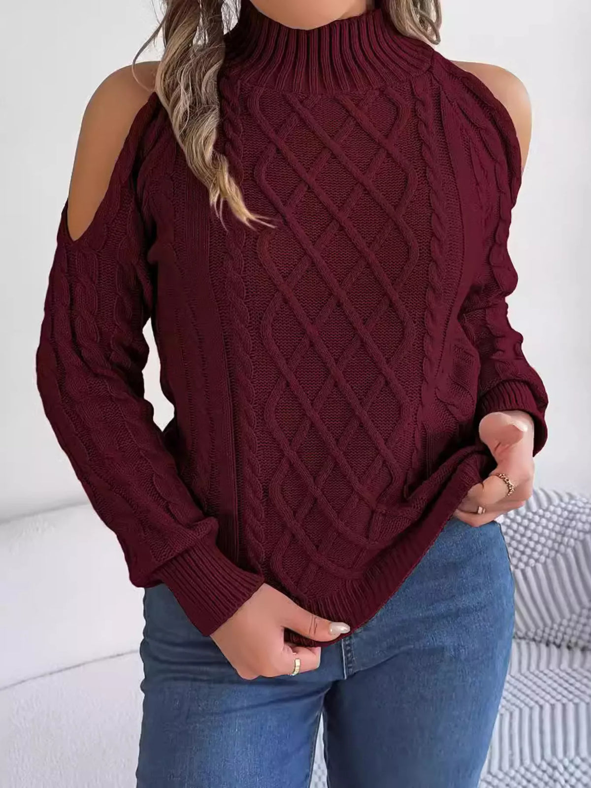 Burgundy cold-shoulder cable-knit sweater, front holding hem.