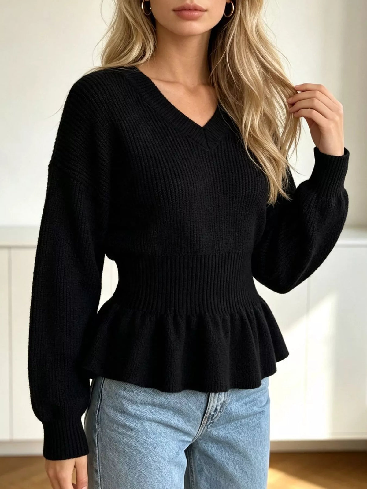 Black v-neck peplum-hem knit sweater, front with raised hand.