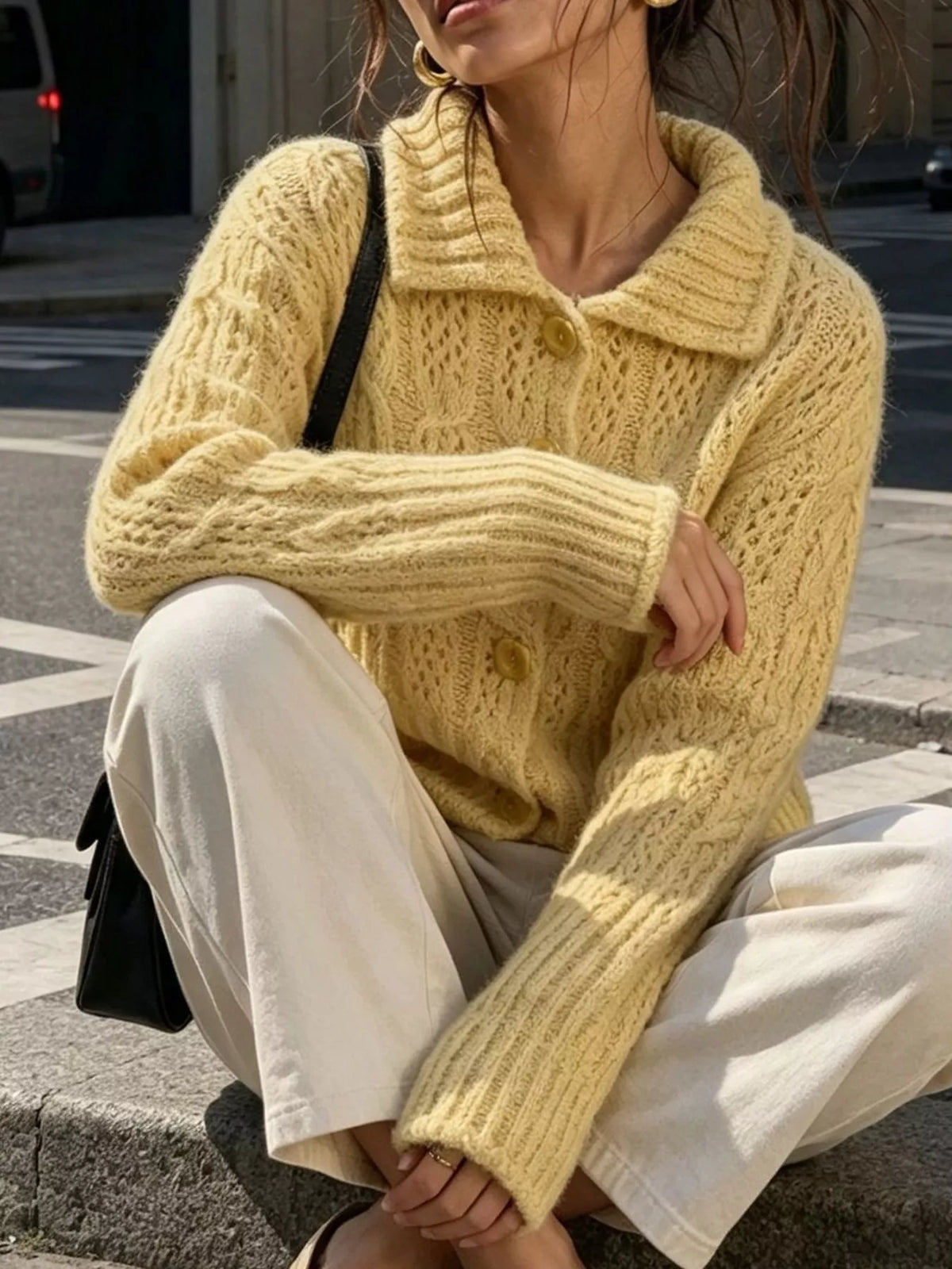 Yellow cable-knit collared button-front cardigan, seated front view.