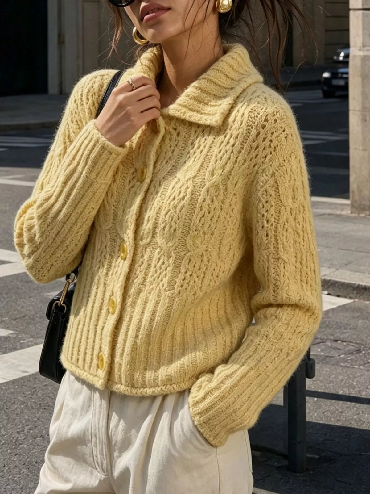 Yellow cable-knit collared button-front cardigan, front holding collar.