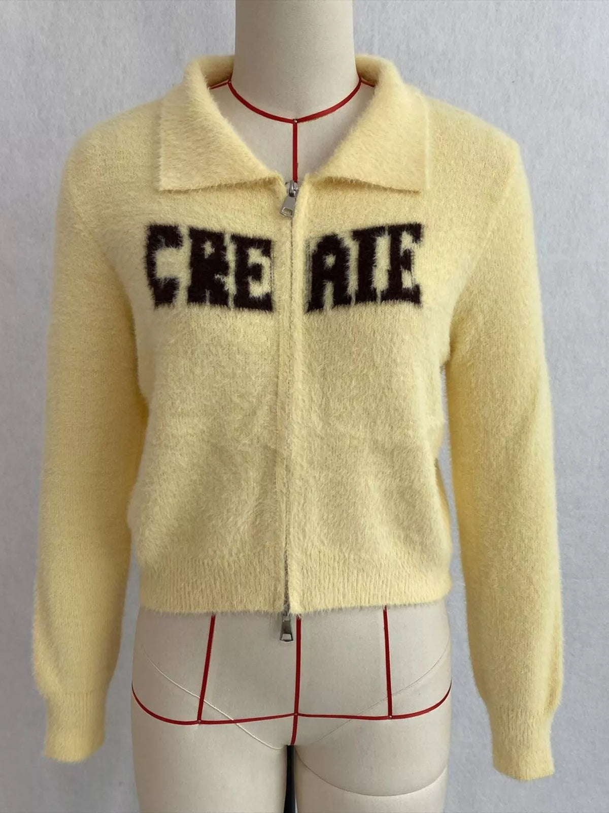 Yellow fuzzy letter zip-up cardigan, front on dress form.
