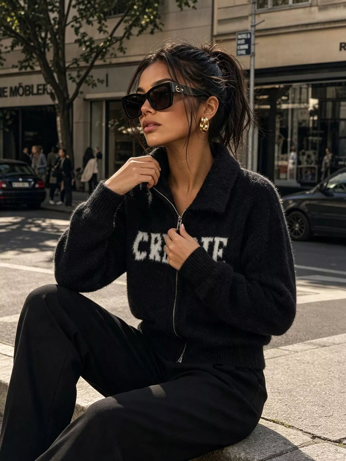 Black fuzzy letter zip-up cardigan, seated front view.