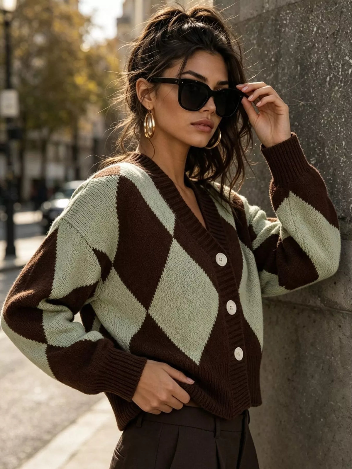 Brown and green argyle v-neck button-front cardigan, front with raised hand.