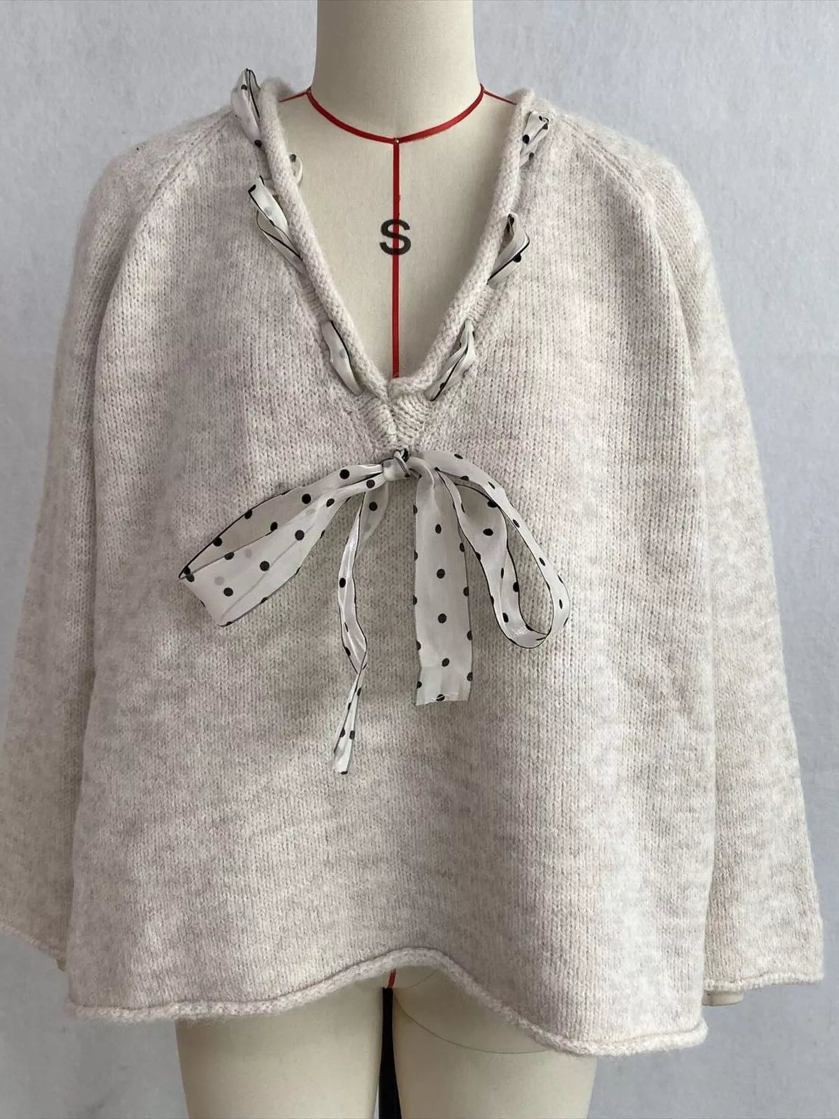 Beige v-neck knit top with polka dot ribbon tie, front on dress form.
