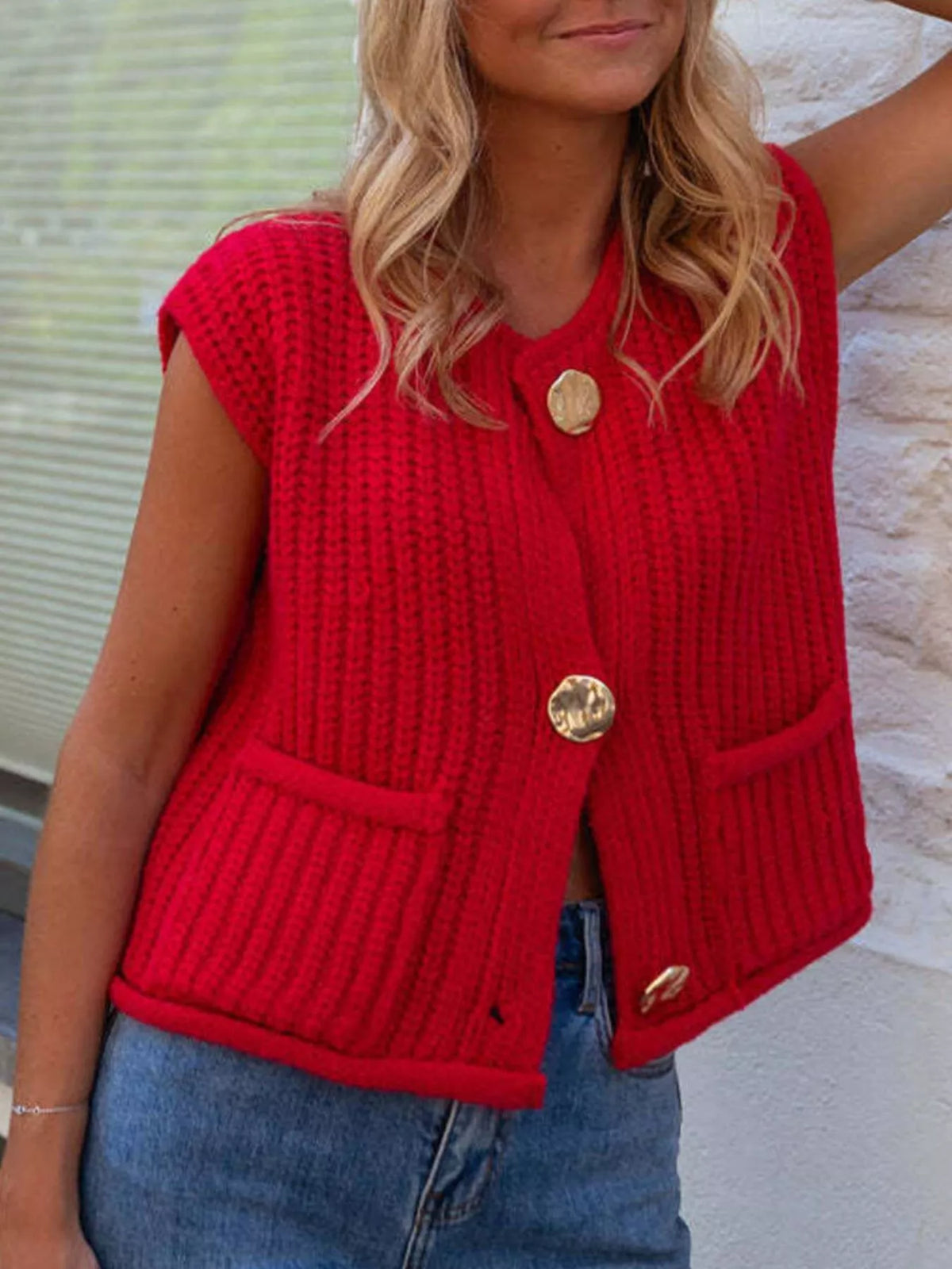 Red button-front knit sweater vest, front view with raised arm.