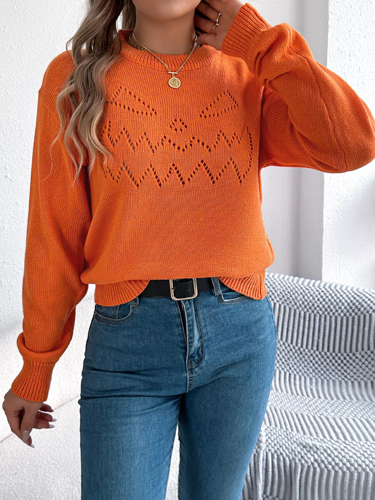 Orange halloween pumpkin face knit sweater, front with raised hand.