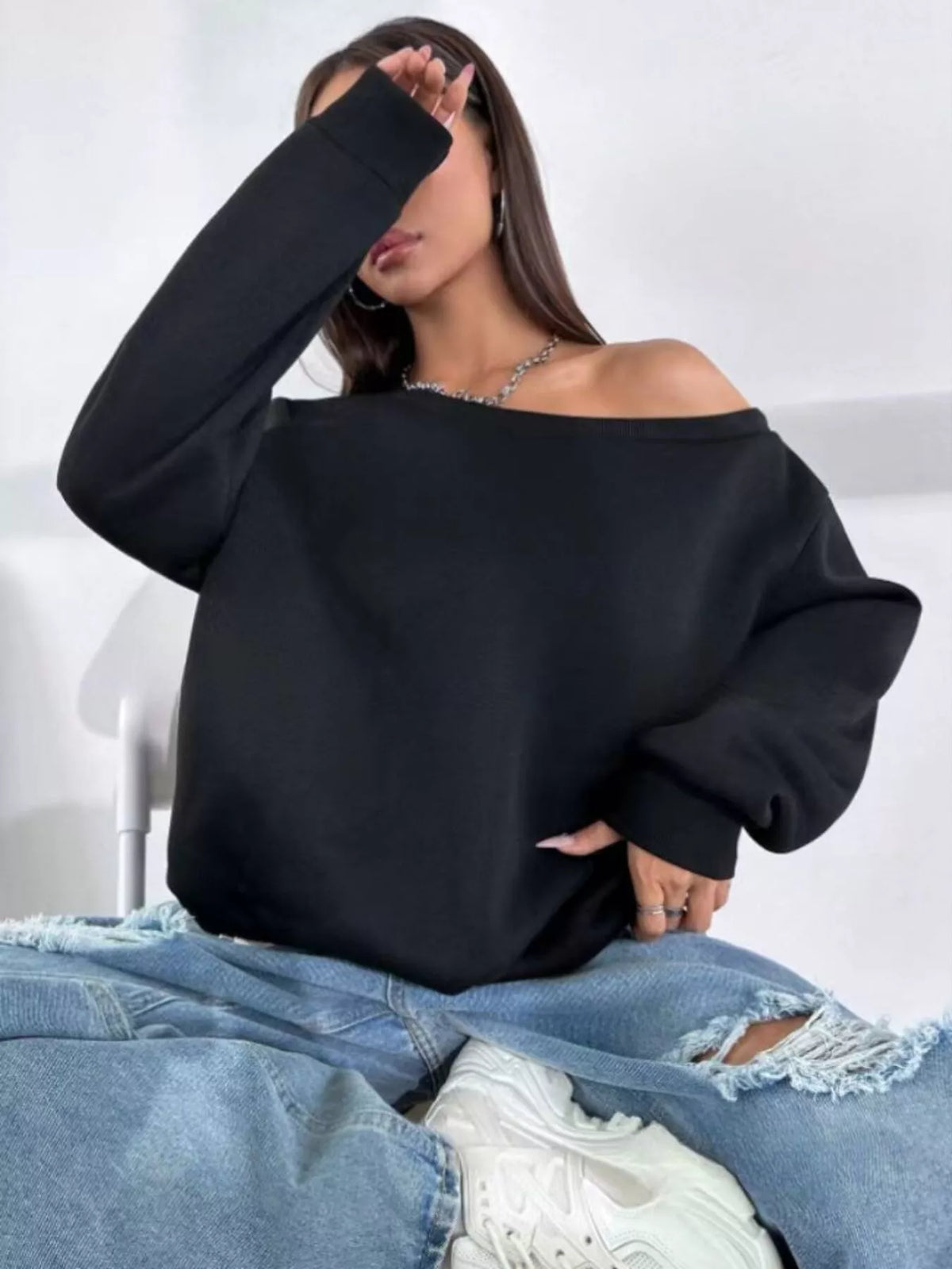 Black asymmetric-neck sweatshirt, seated front view with arm raised