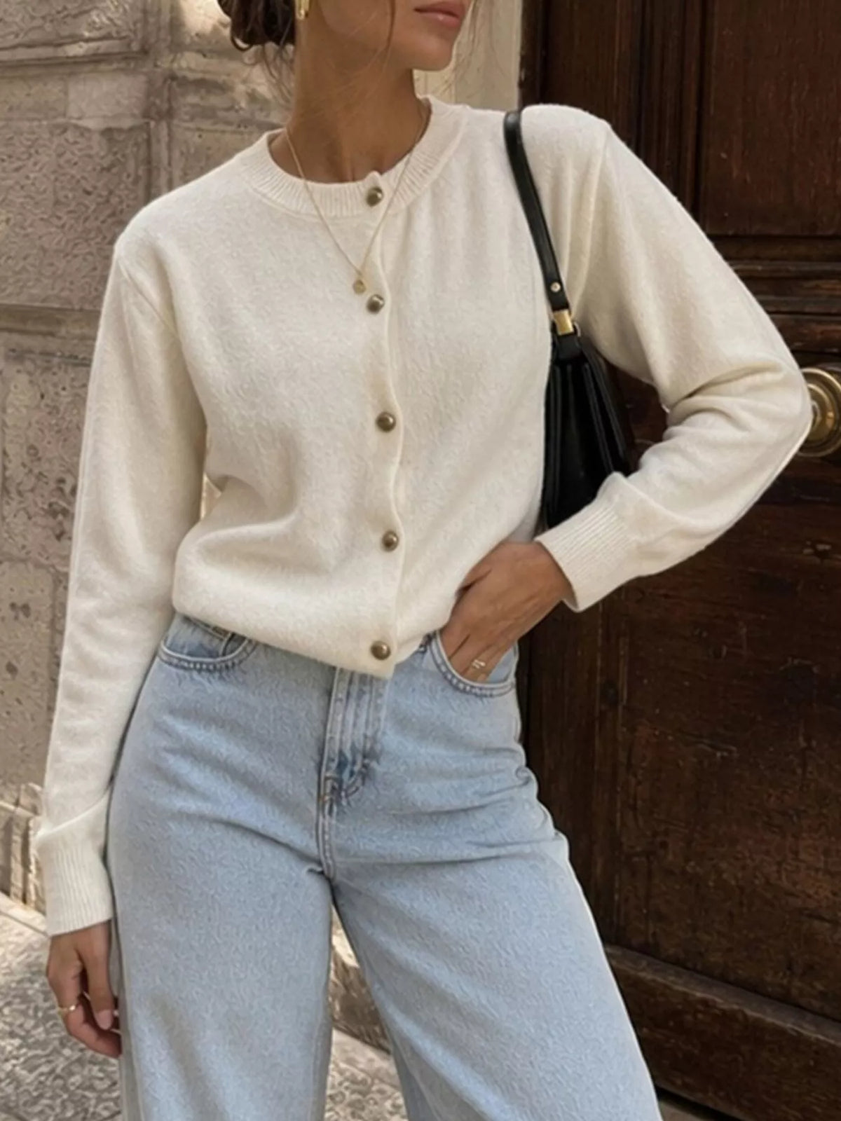 White round-neck button-front knit cardigan, front view with hand at waist.