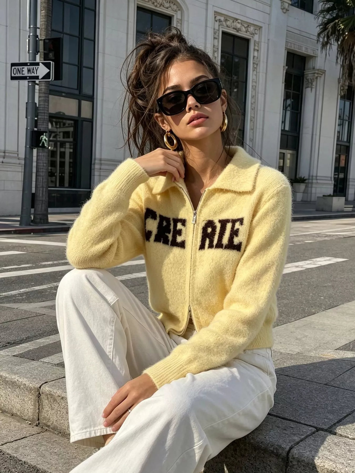 Yellow fuzzy letter zip-up cardigan, seated front view.