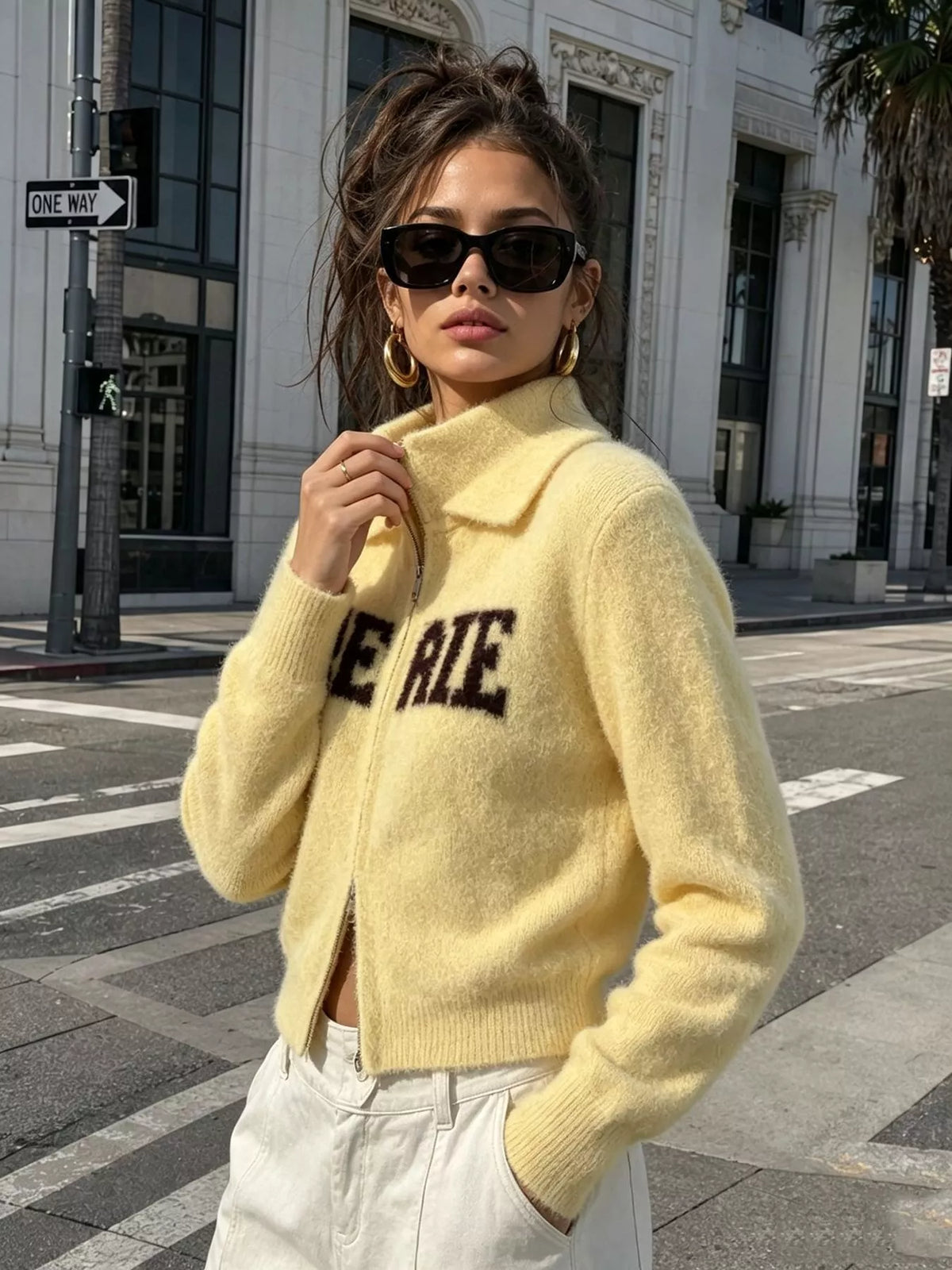 Yellow fuzzy letter zip-up cardigan, front holding collar.