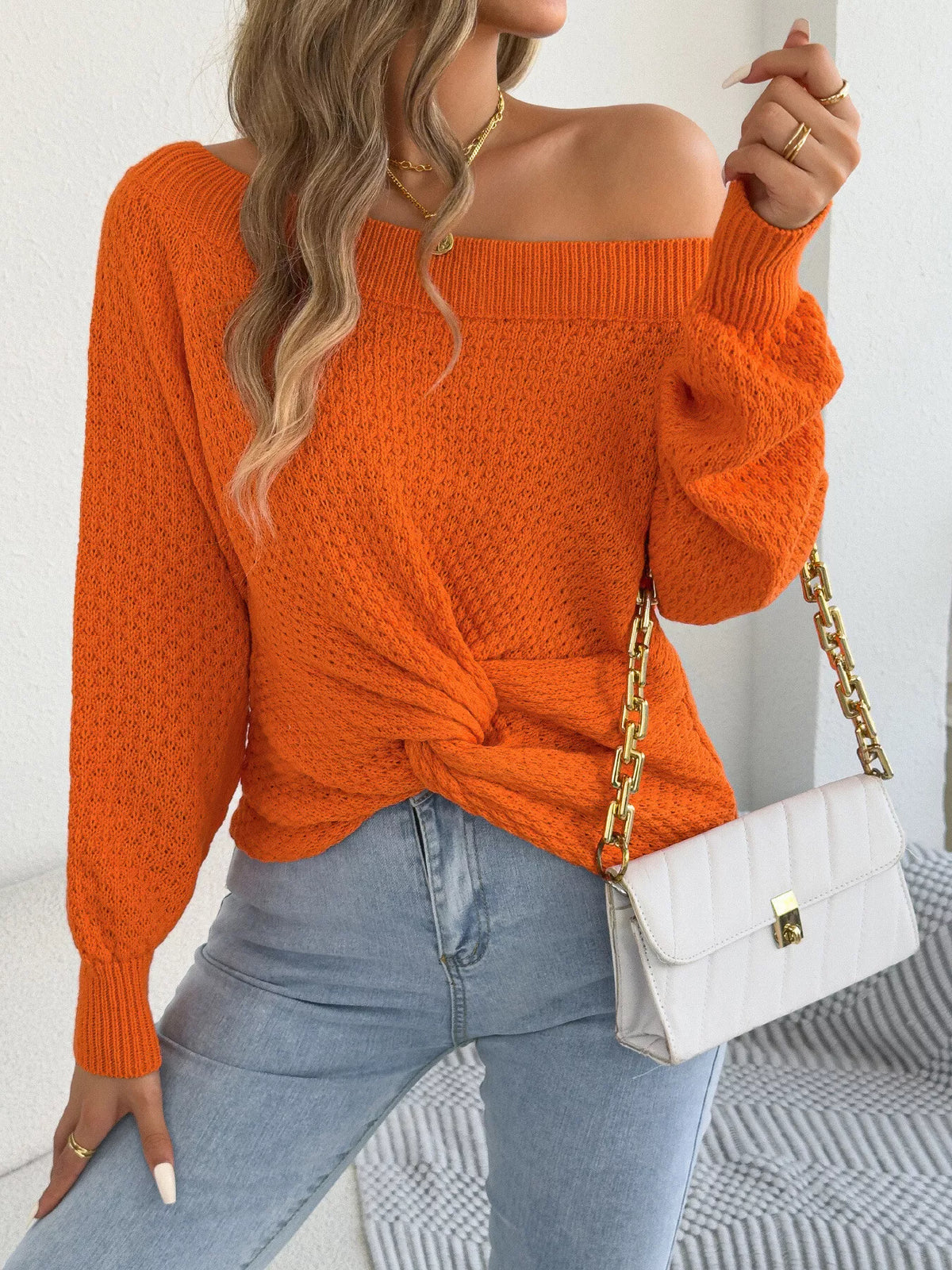 Orange off-shoulder twist-front knit sweater, front view with bent arm.