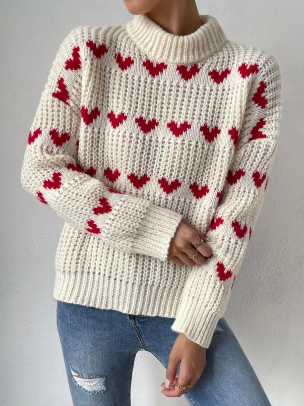 Cream and red heart-pattern chunky-knit sweater, front view with arm across waist
