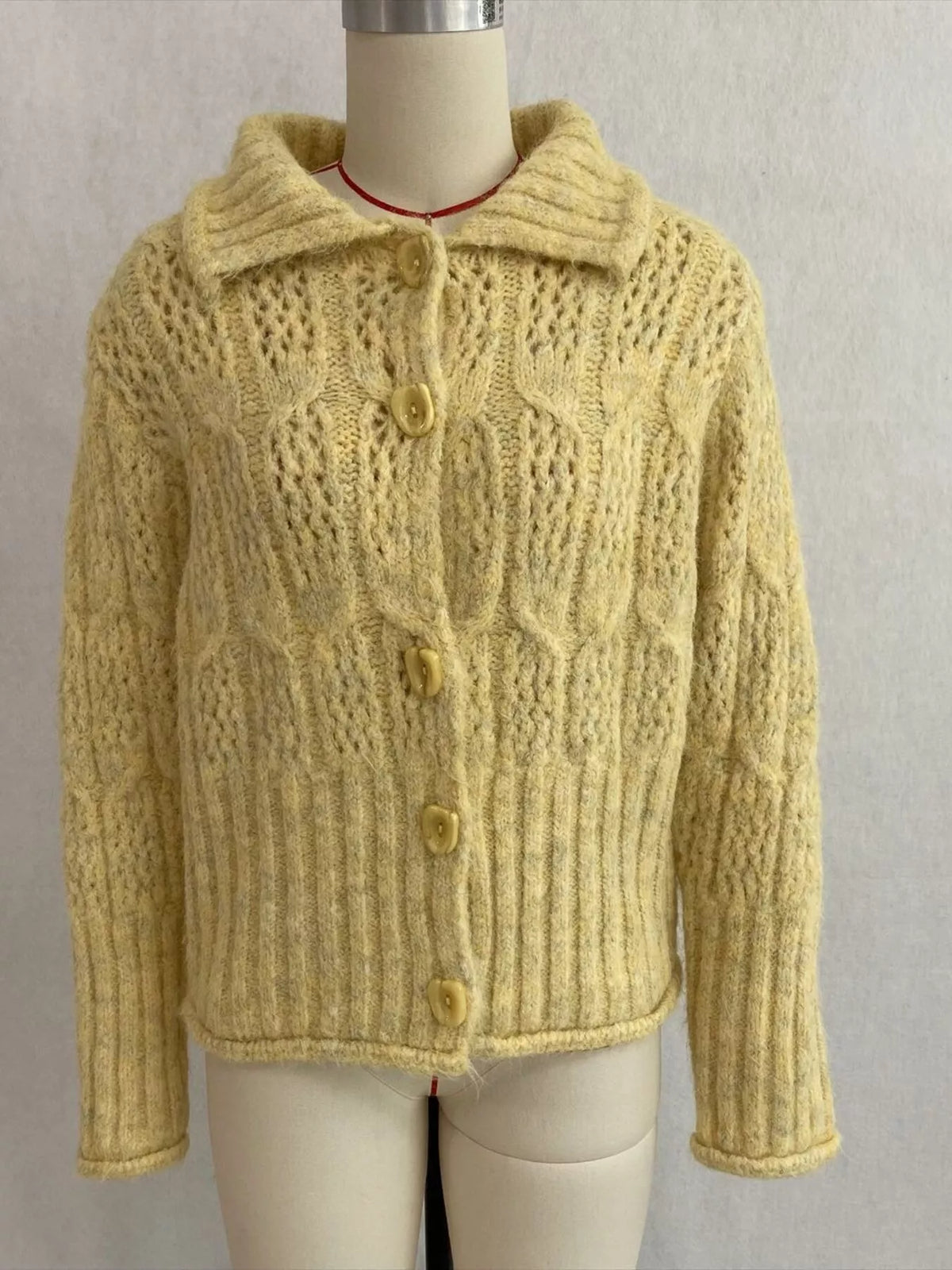 Yellow cable-knit collared button-front cardigan, front on dress form.