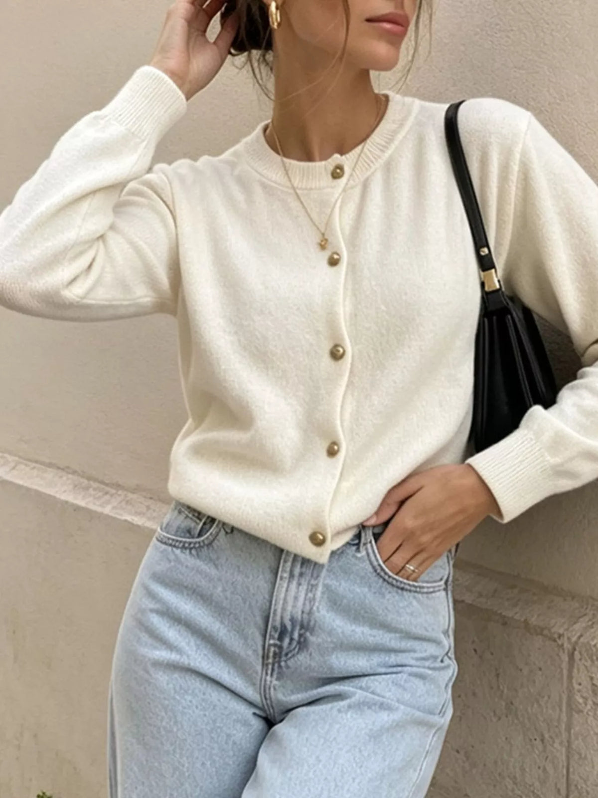 White round-neck button-front knit cardigan, front view with raised hand.