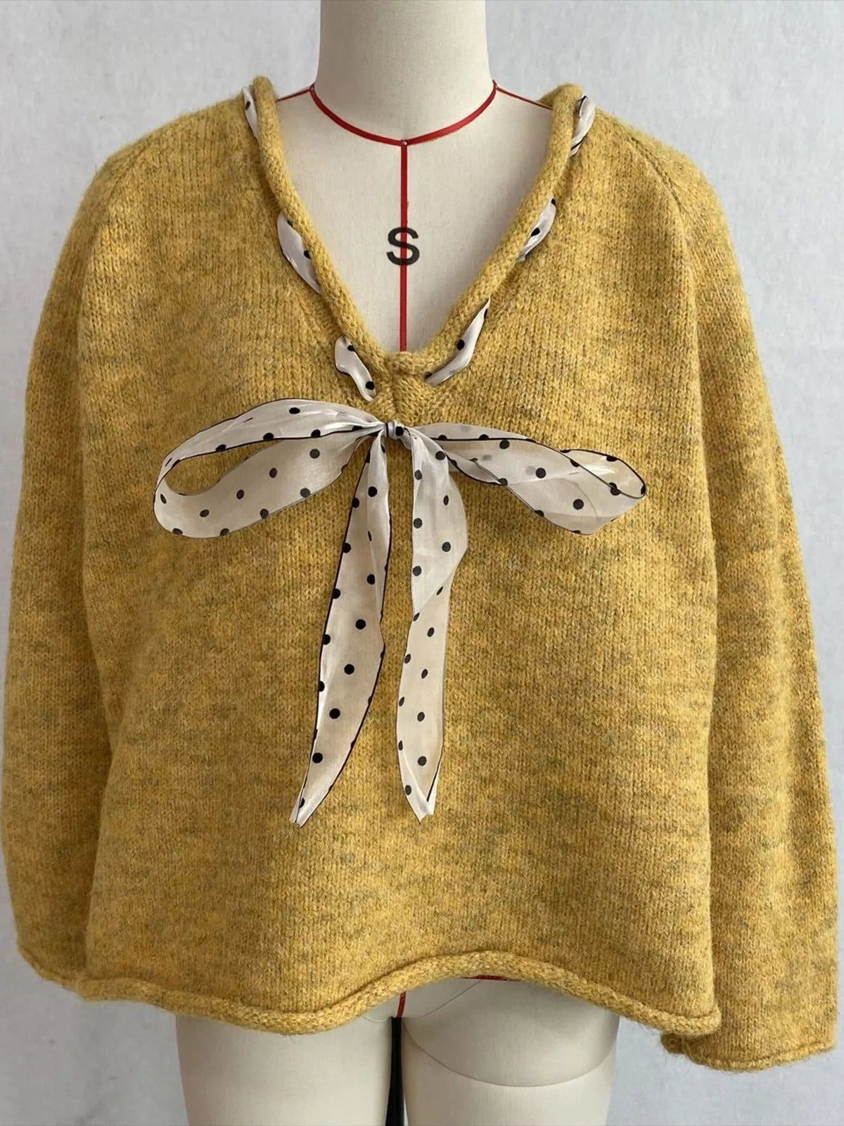 Yellow v-neck knit top with polka dot ribbon tie, front on dress form.