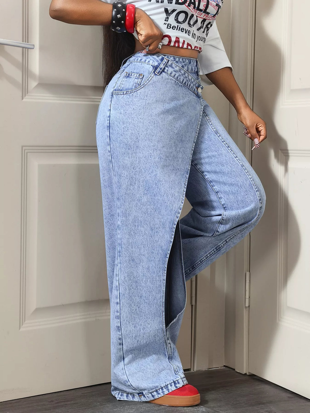 Light blue asymmetric-wrap wide-leg jeans, side view with one knee bent