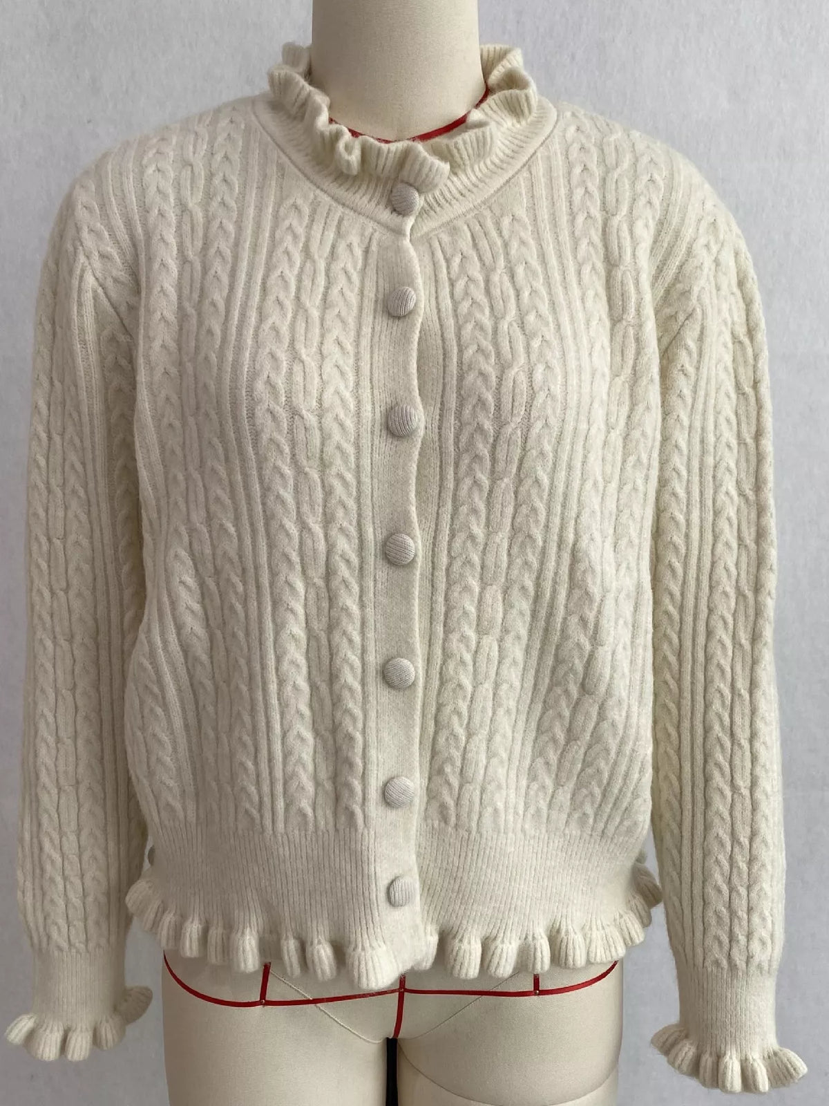 Ivory cable-knit ruffle-trim cardigan, front on dress form.