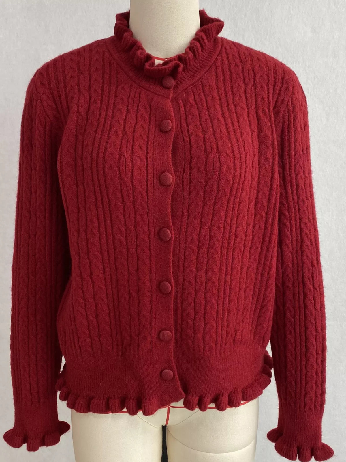 Burgundy cable-knit ruffle-trim cardigan, front on dress form.
