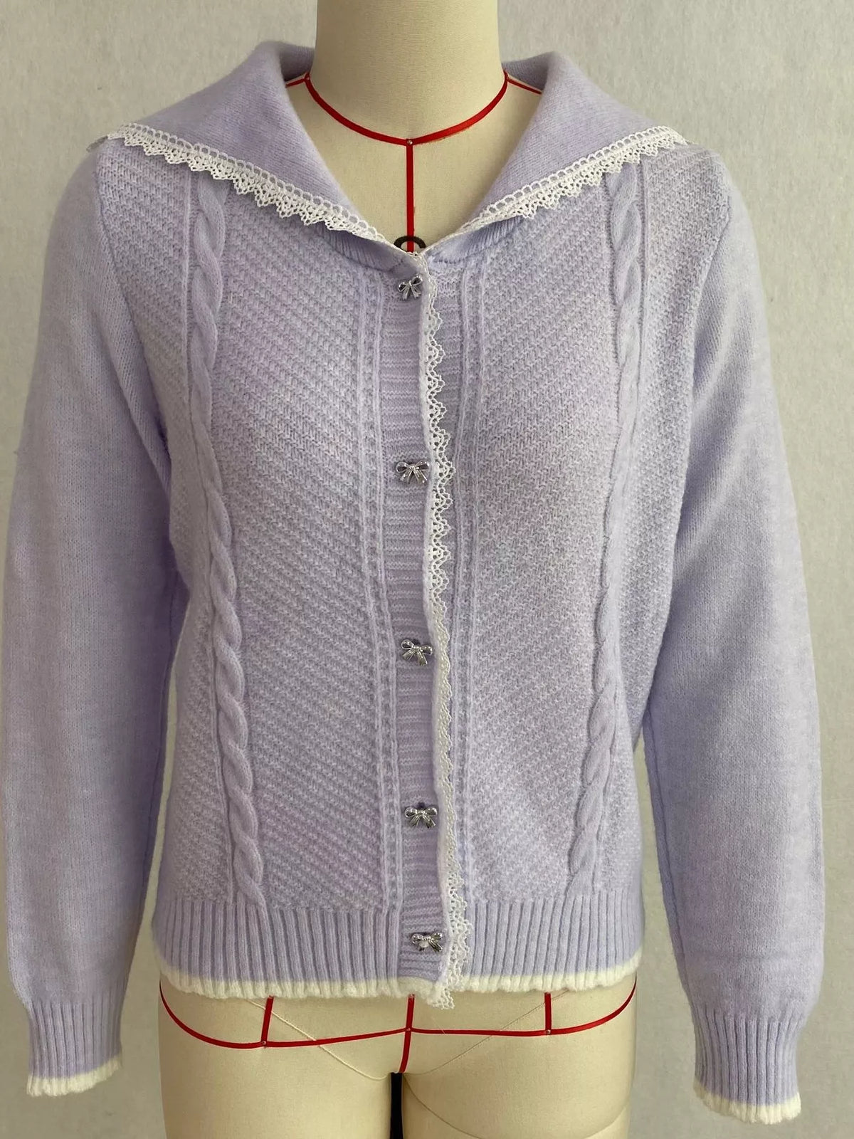 Lavender cable-knit cardigan with lace trim, front on dress form.
