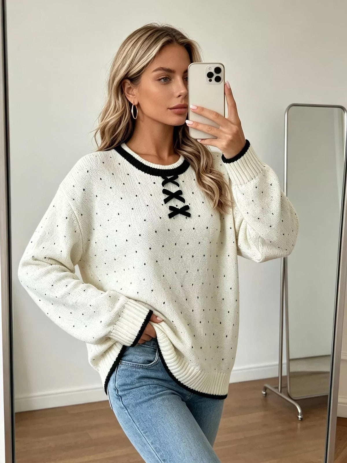 White and black polka dot lace-up sweater, front view with raised hand.