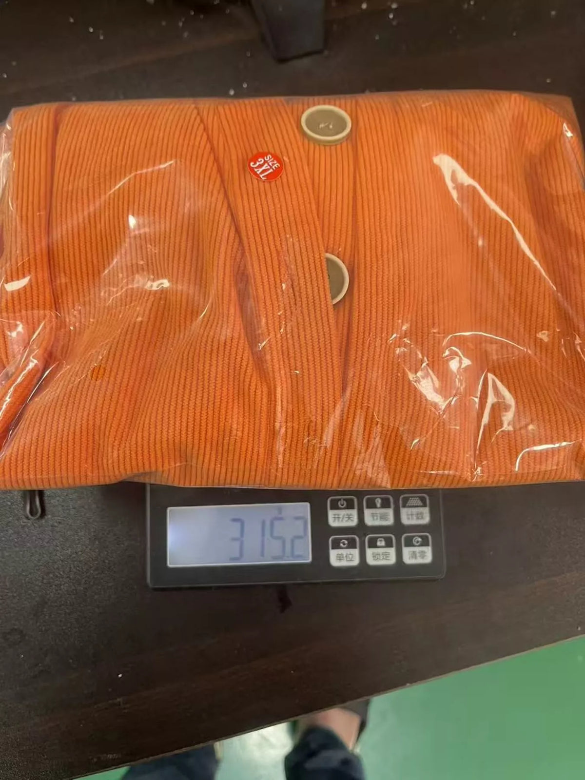 Orange button-detail top in supplier packaging on a scale