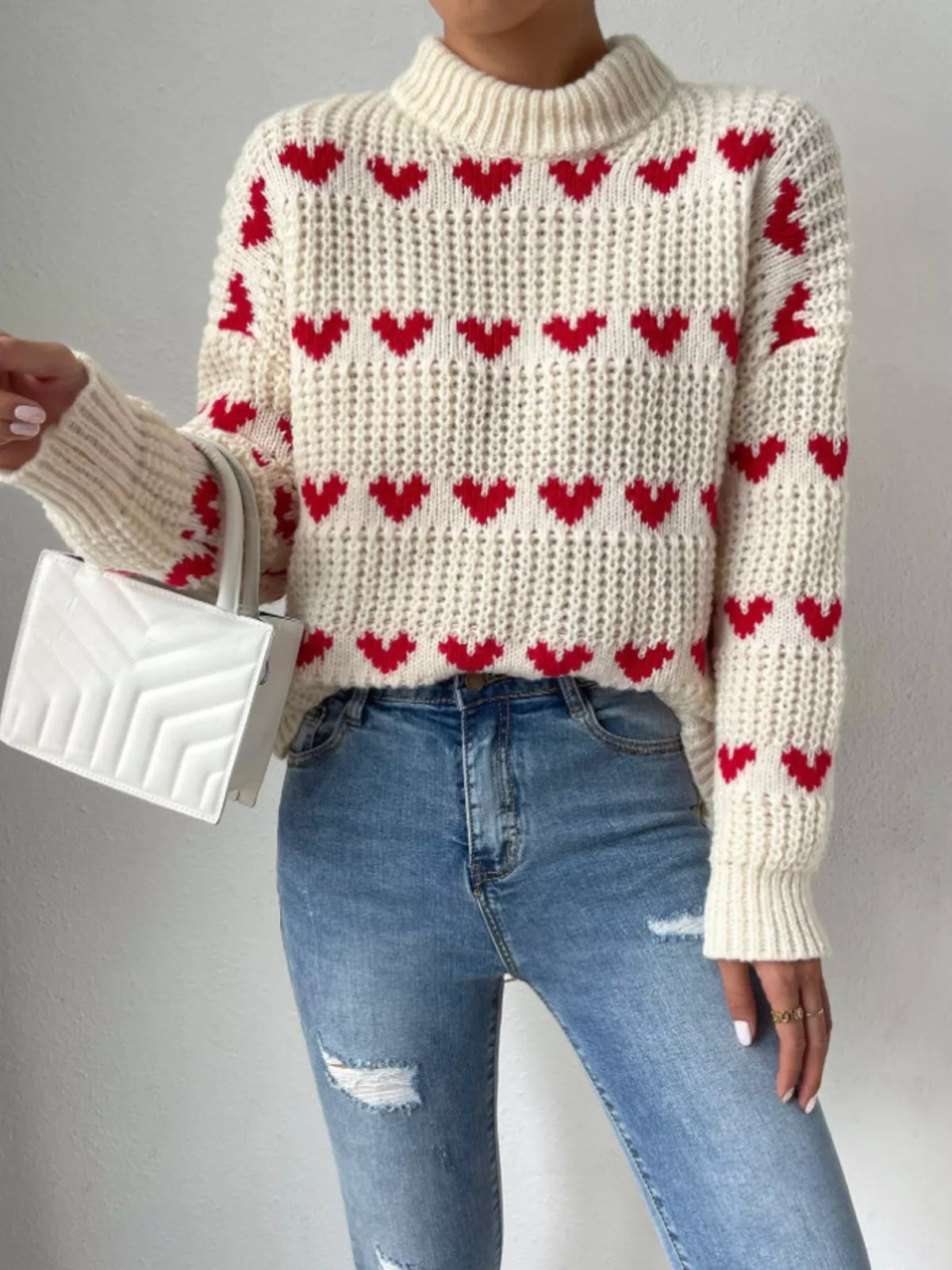 Cream and red heart-pattern chunky-knit sweater, front view with handbag