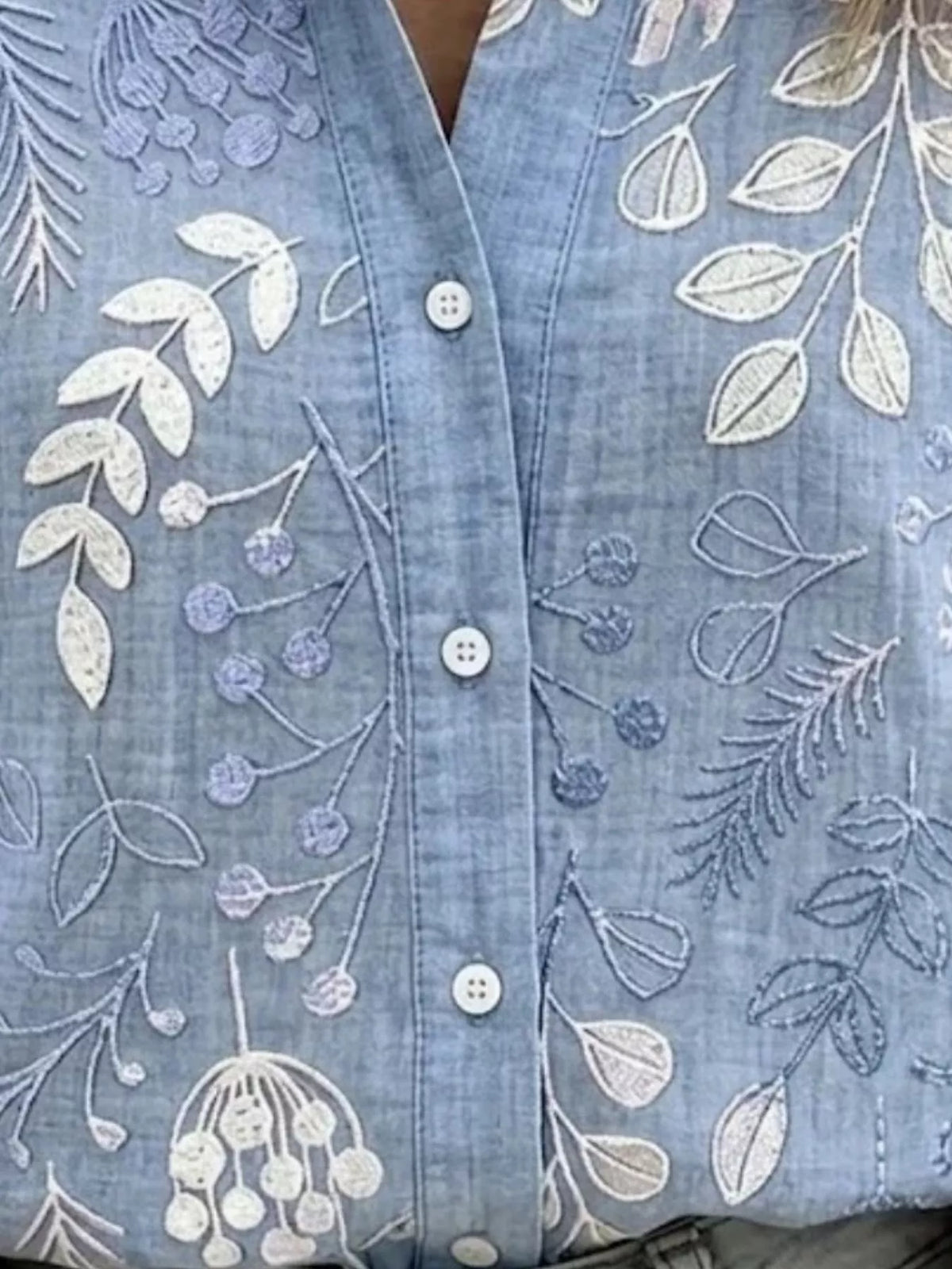 Blue leaf-embroidered button-down shirt, leaf embroidery and button detail.