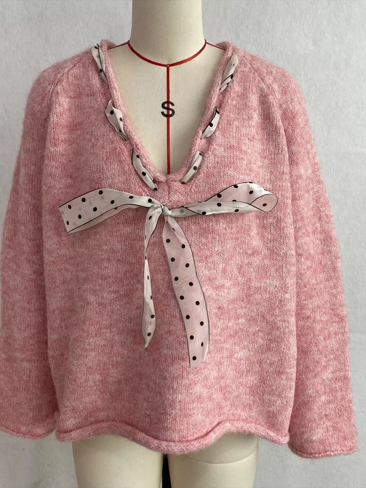 Pink v-neck knit top with polka dot ribbon tie, front on dress form.