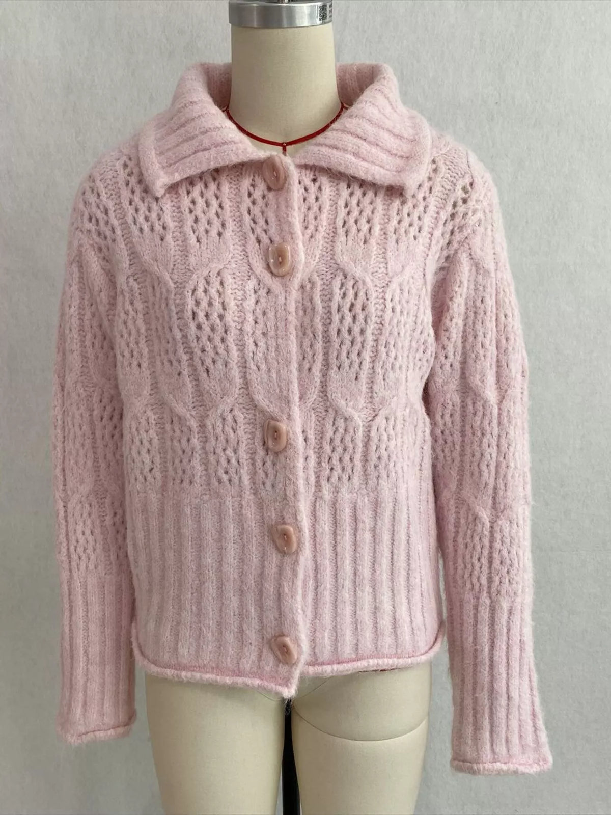 Pink cable-knit collared button-front cardigan, front on dress form.