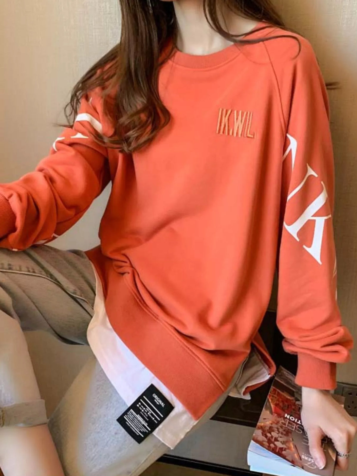 Orange layered-hem sweatshirt with graphic sleeve detail, back view