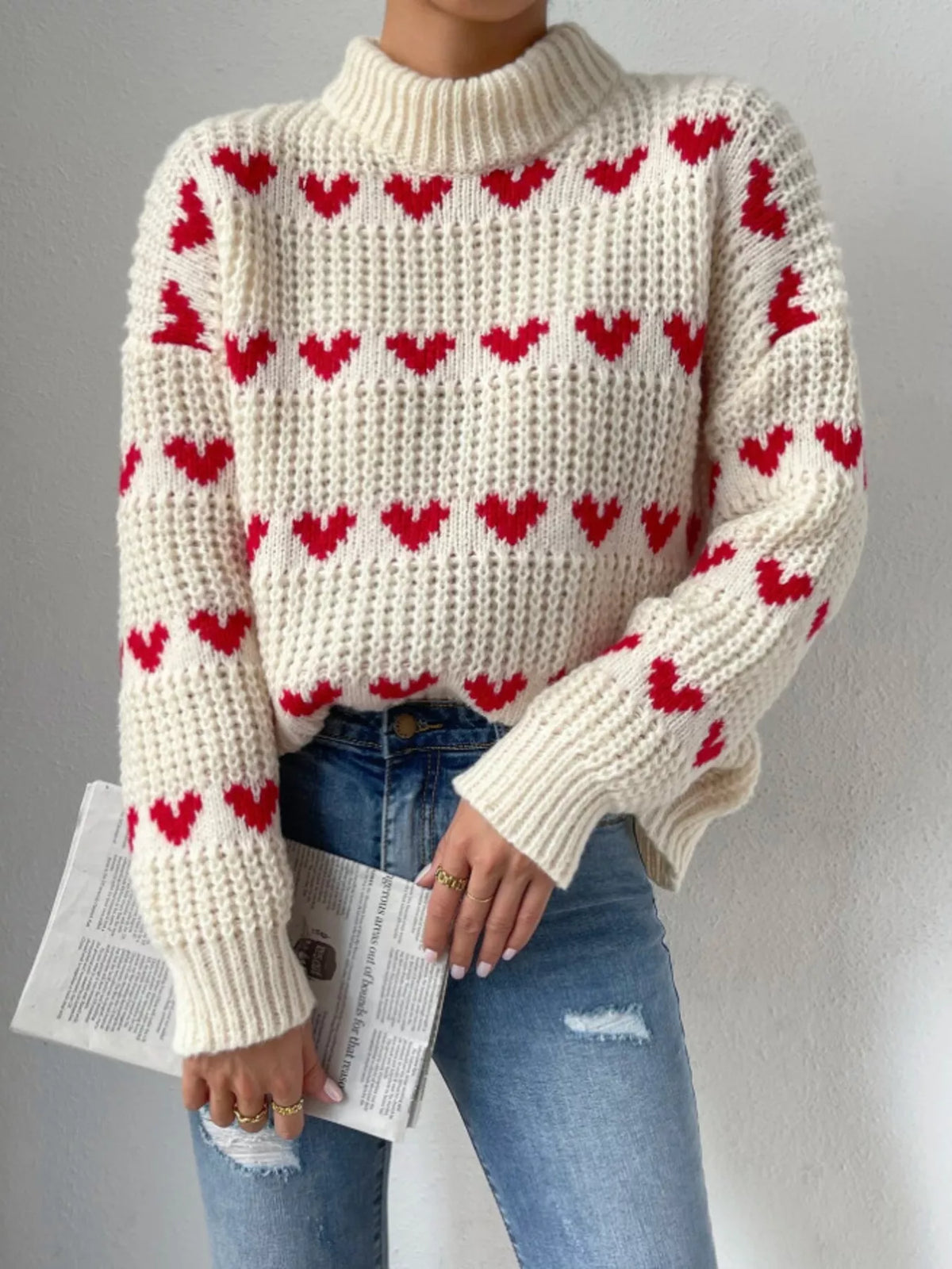 Cream and red heart-pattern chunky-knit sweater, front view with newspaper