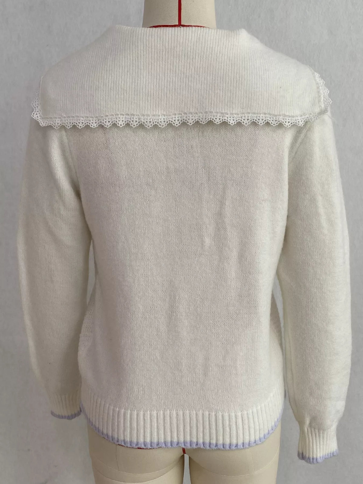 White cable-knit cardigan with lace trim, back on dress form.
