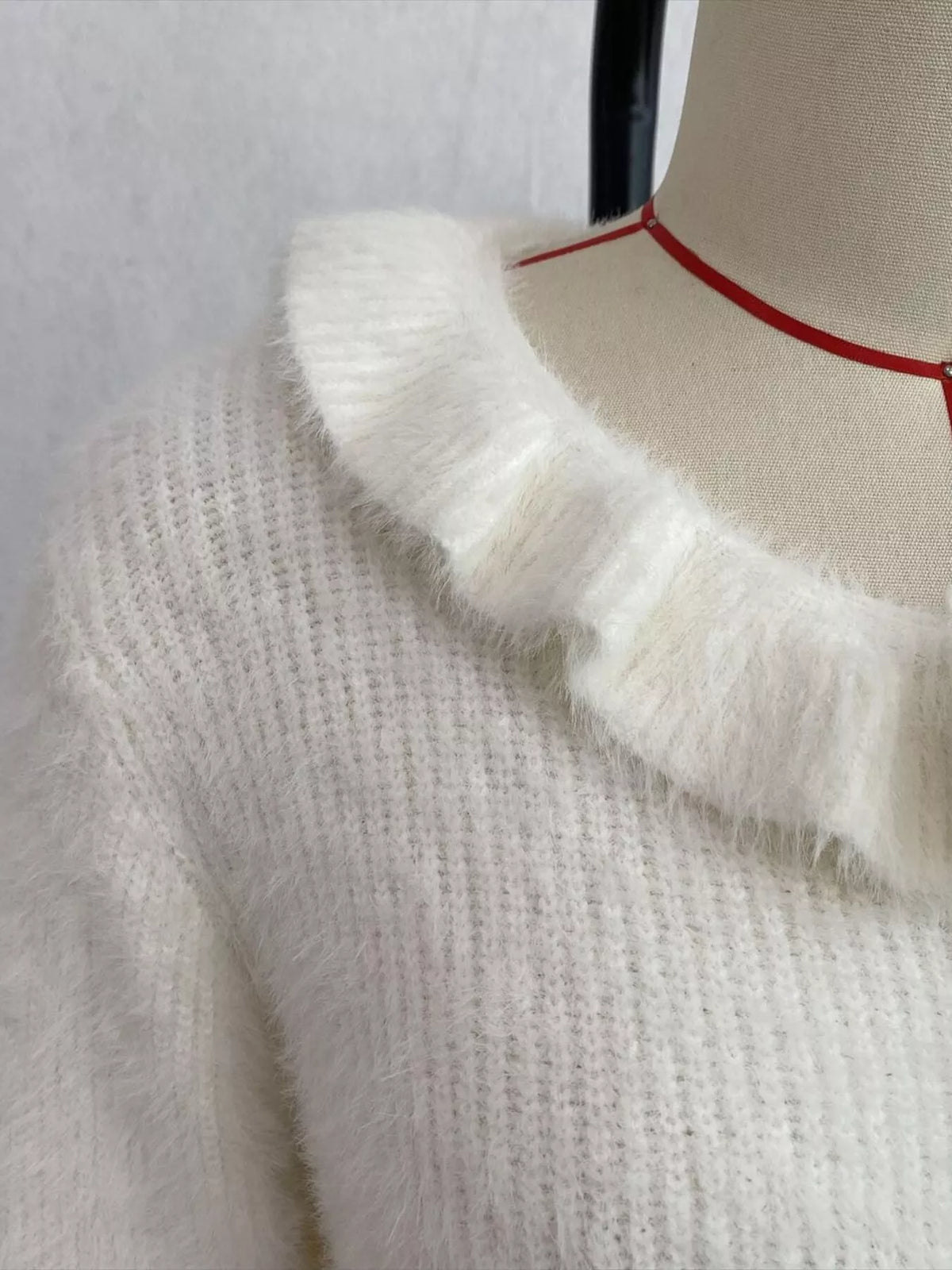 Ivory fuzzy ruffle-trim button-front cardigan, ruffled collar detail.