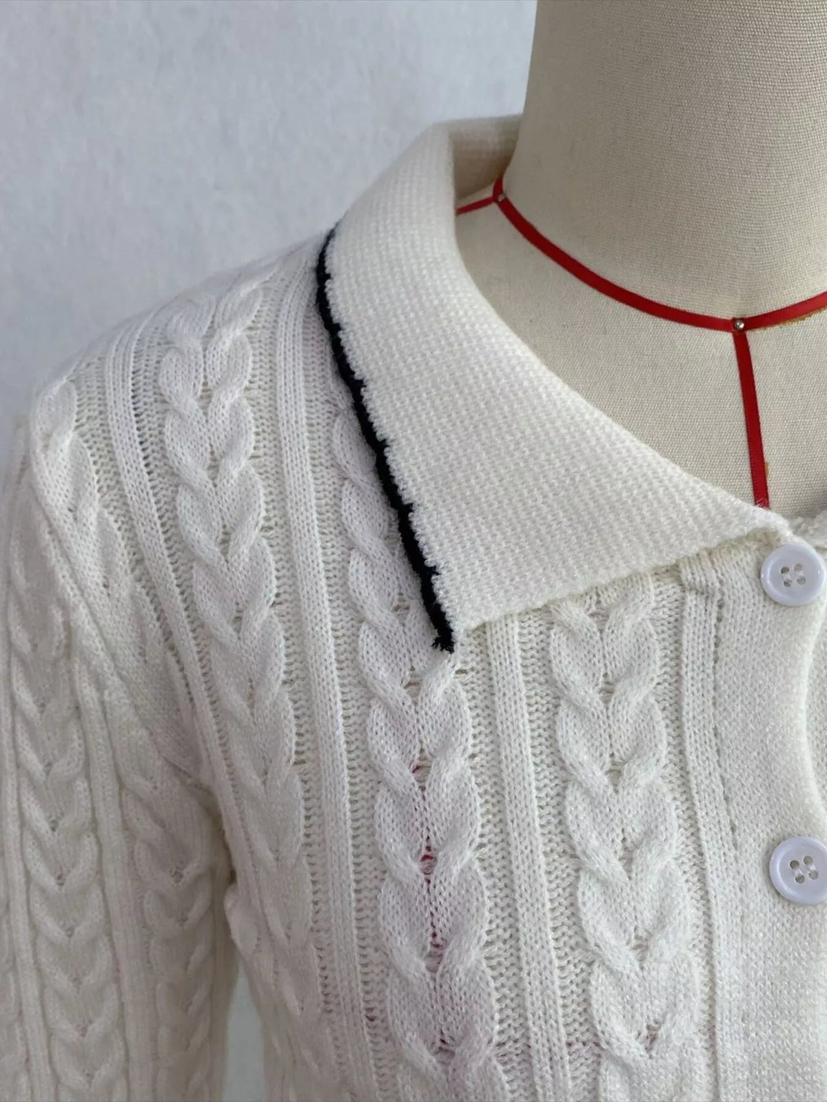 Ivory cable-knit polo-collar cardigan, collar and button detail.