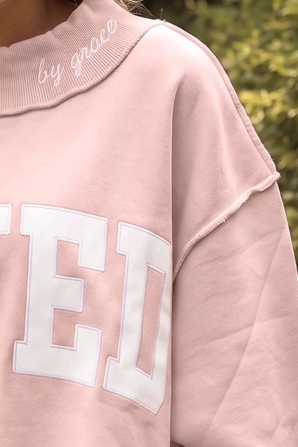 Pink SAVED graphic sweatshirt, shoulder seam and lettering close-up