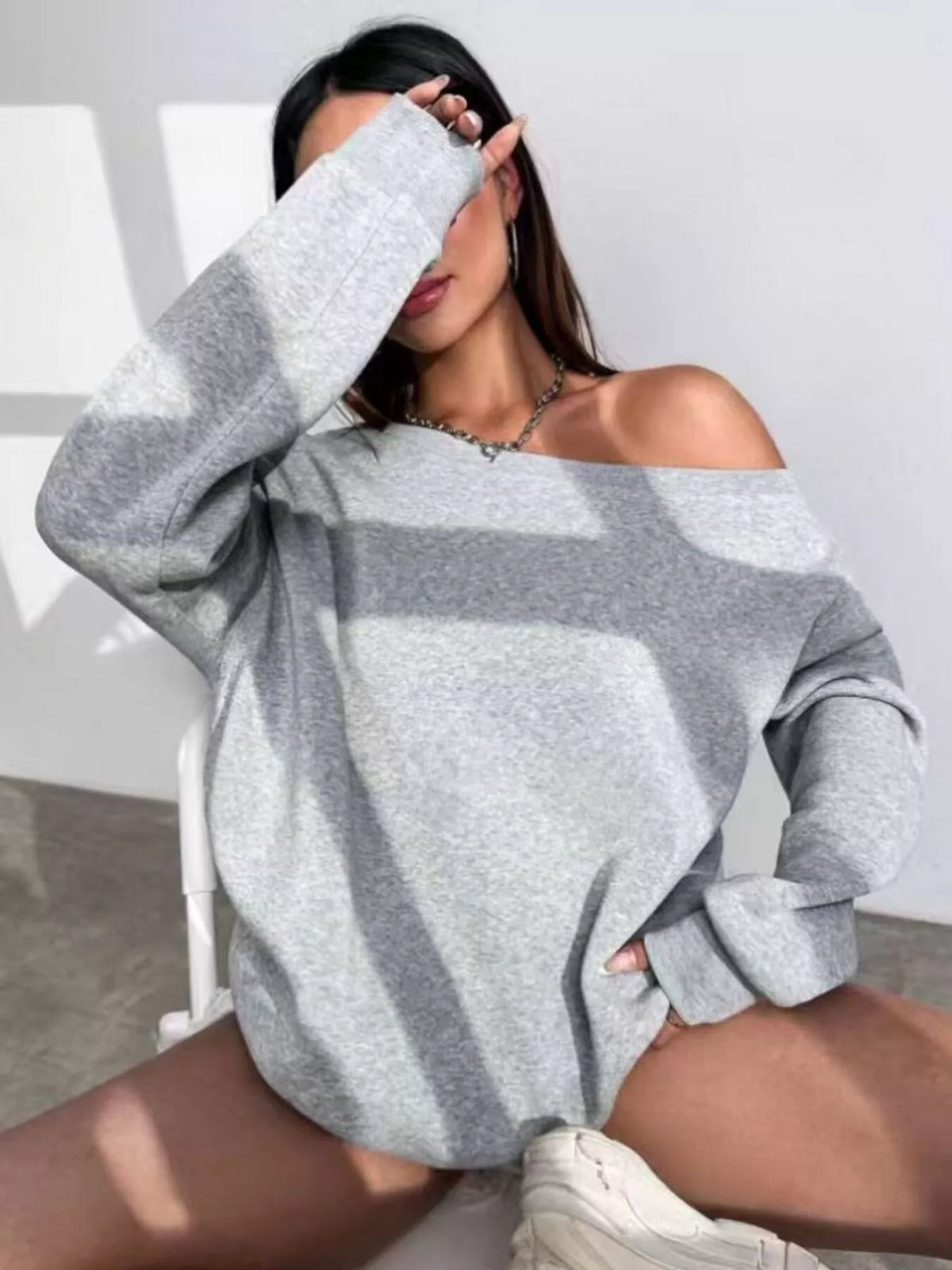 Gray asymmetric-neck sweatshirt, seated front view with arm raised