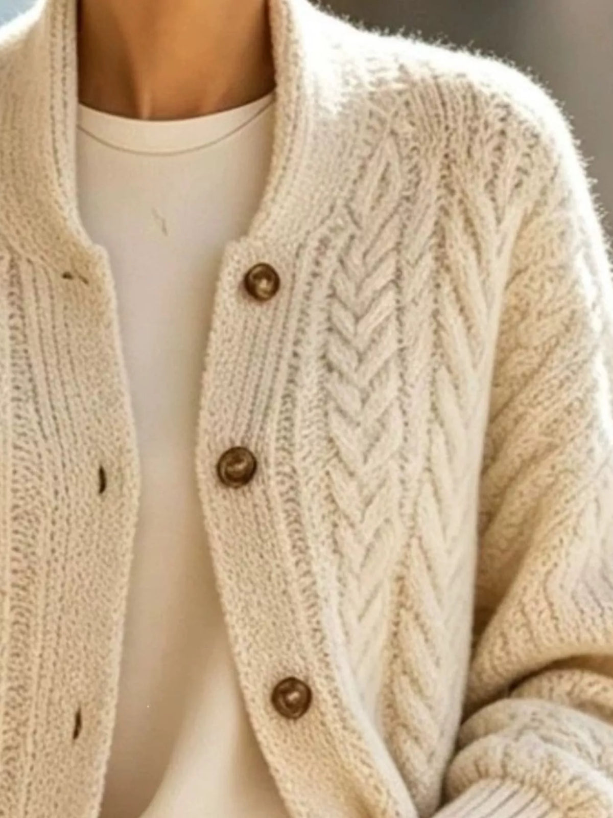 Ivory longline cable-knit button-front cardigan, cable knit and button detail.